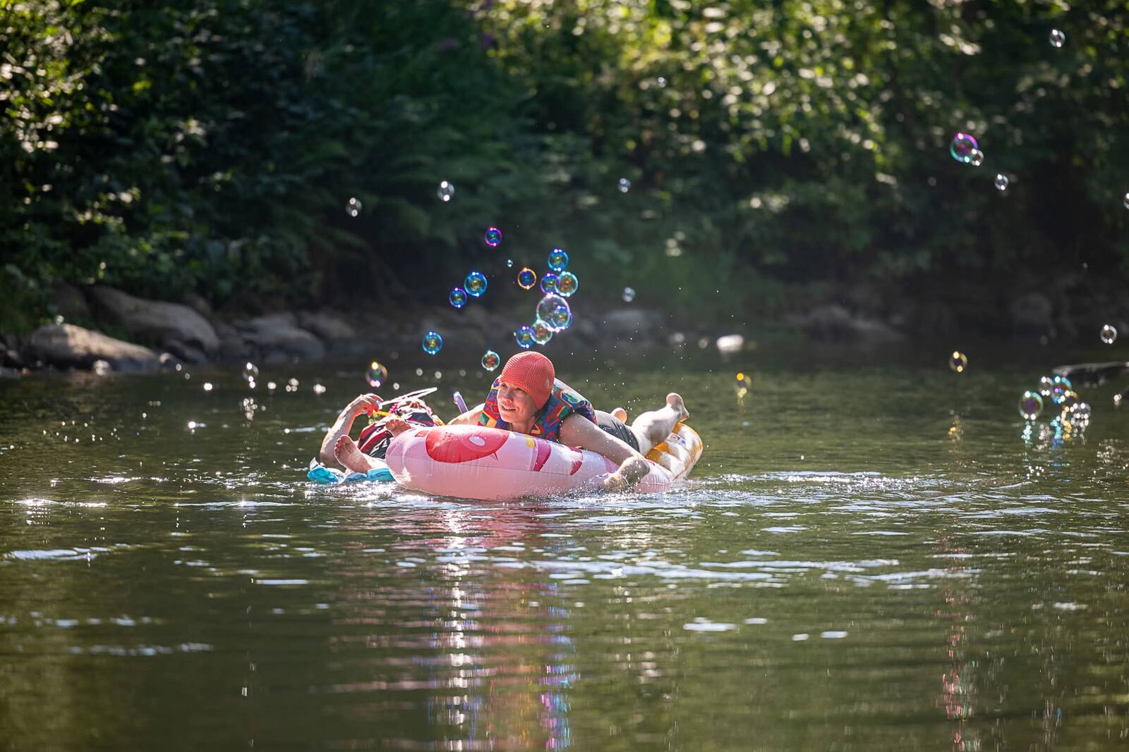Leende floatare i rosa badring bland såpbubblor på Umeälven